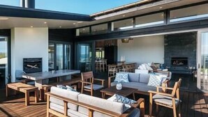A modern outdoor living area with a wooden deck, a sofa, a dining table, and chairs. - Tradewinds Estate by Waiheke Pure - Commanding views, pool, hot tub, grand open planned living, sun soaked decks (Waiheke Island)