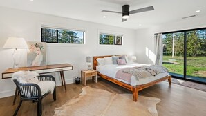 A bedroom with a bed, desk, chair, and large windows.