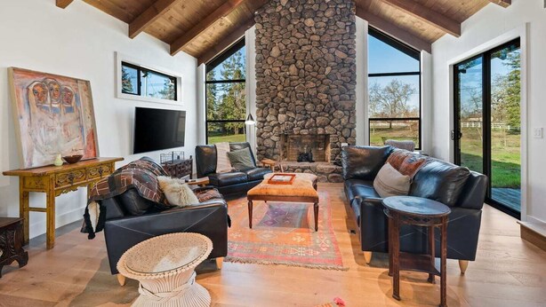 A spacious living room with a stone fireplace, leather sofas, and large windows offering views of the outdoors.