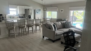 A modern living room with a sofa, chairs, and a dining area with a kitchen in the background.