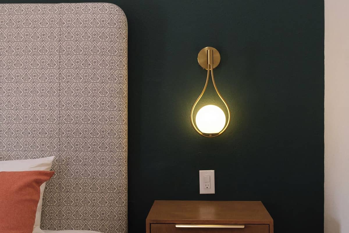 Un dormitorio con cabecera estampada, mesita de noche con cajones e iluminación empotrada en la pared.