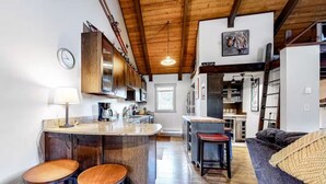 Une cuisine spacieuse avec des meubles en bois, un îlot central doté de tabourets et un coin repas comprenant un canapé et une lampe.