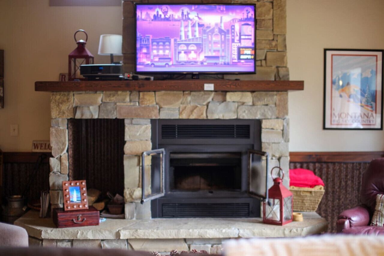 Una chimenea de piedra con un televisor encima, un farolillo rojo y un cuadro en el manto.