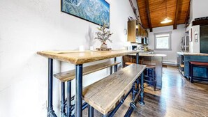 Une cuisine rustique avec des tuyaux apparents, des bancs en bois et un grand tableau accroché au mur.
