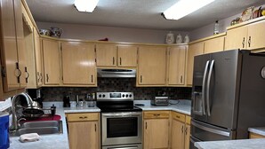 Una cocina con armarios de madera, una estufa de acero inoxidable, un refrigerador y piso de baldosas.
