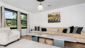 A living room with a beige sofa, a white armchair, a coffee table, and a painting on the wall.