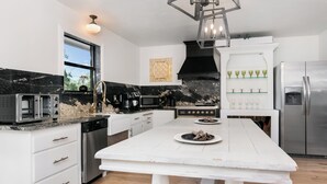 A modern kitchen with a white island, stainless steel appliances, and a black marble backsplash.