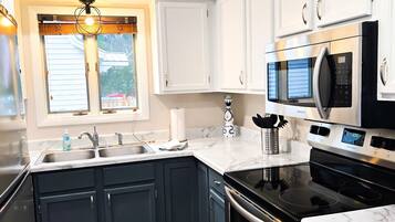 A modern kitchen with dark blue cabinets, a black stove, a microwave, and a sink.