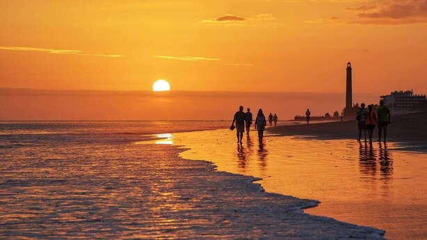 A sunset over a beach with people walking along the shore.