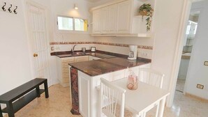 A kitchen with white cabinets, a marble countertop, and a dining area with a white table and chairs.