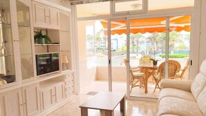 A living room with a sofa, a TV, a table, and a balcony with outdoor furniture.
