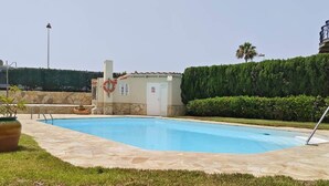 A rectangular swimming pool with a tiled deck, surrounded by a well-maintained lawn and a hedge.
