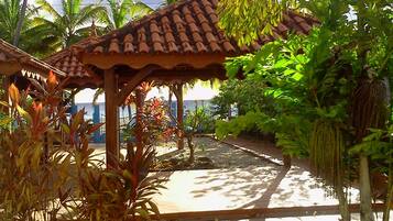 A covered outdoor area with a tiled roof, surrounded by tropical vegetation and palm trees.