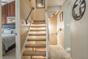Un escalier dont les marches sont recouvertes de moquette, menant à une chambre à coucher équipée d’un lit et d’une tête de lit.