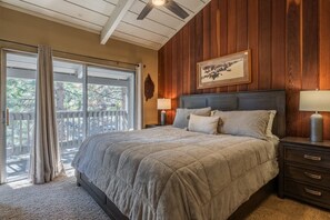 Een slaapkamer met een groot bed, houten paneelwanden, een plafondventilator en uitzicht door een schuifdeur.
