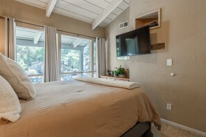 Un dormitorio con una cama grande, un televisor de pantalla plana montado en la pared y vistas al exterior a través de la ventana.