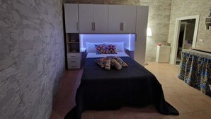 Un dormitorio con cama, armario, mesita de noche y baño visible a través de una puerta abierta.