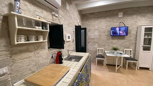 Una cocina con pared de piedra, cafetera, lavabo y televisor mostrando un programa.