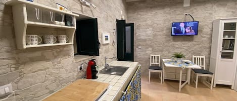 A kitchen with a stone wall, a coffee machine, a sink, and a TV displaying a show.