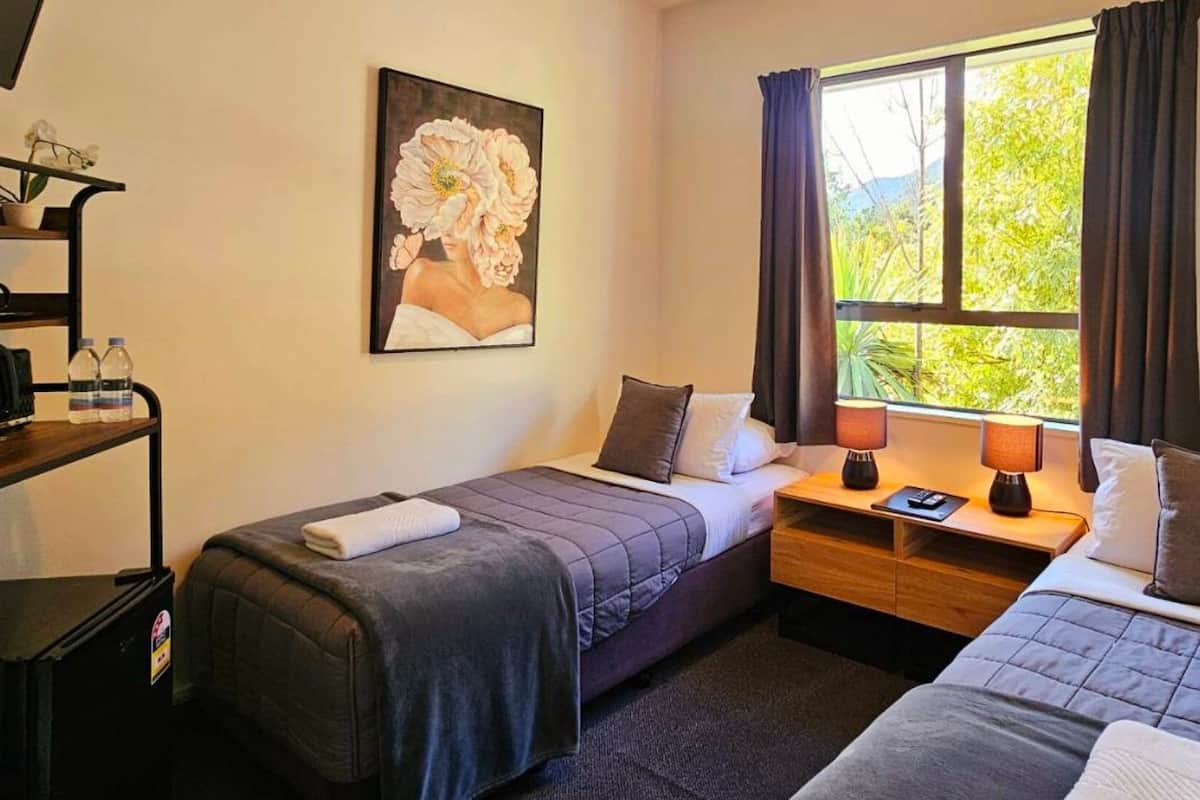 Une chambre d’hôtel avec deux lits, un bureau avec une lampe, un tableau au mur et une fenêtre avec des rideaux.