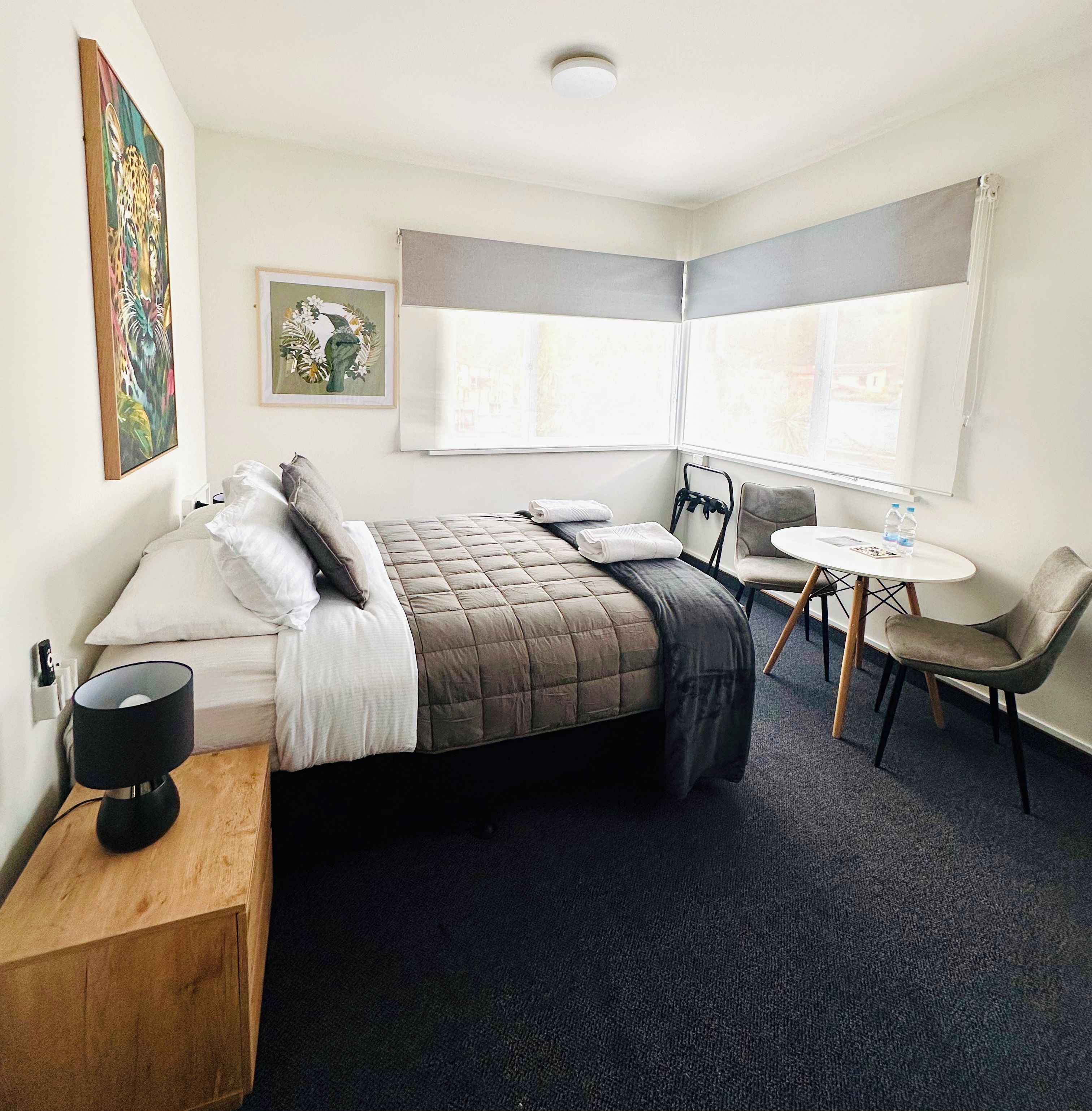 A hotel room with a bed, bedside table, chair, desk, and window.