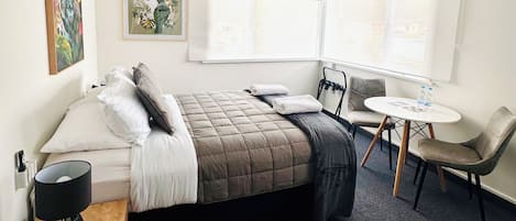 A hotel room with a bed, bedside table, chair, desk, and window.