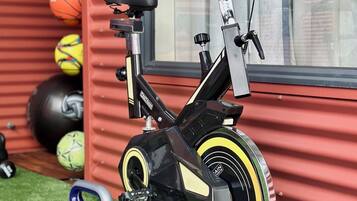 A stationary bike with a water bottle holder, a set of dumbbells, and exercise balls against a red wall.