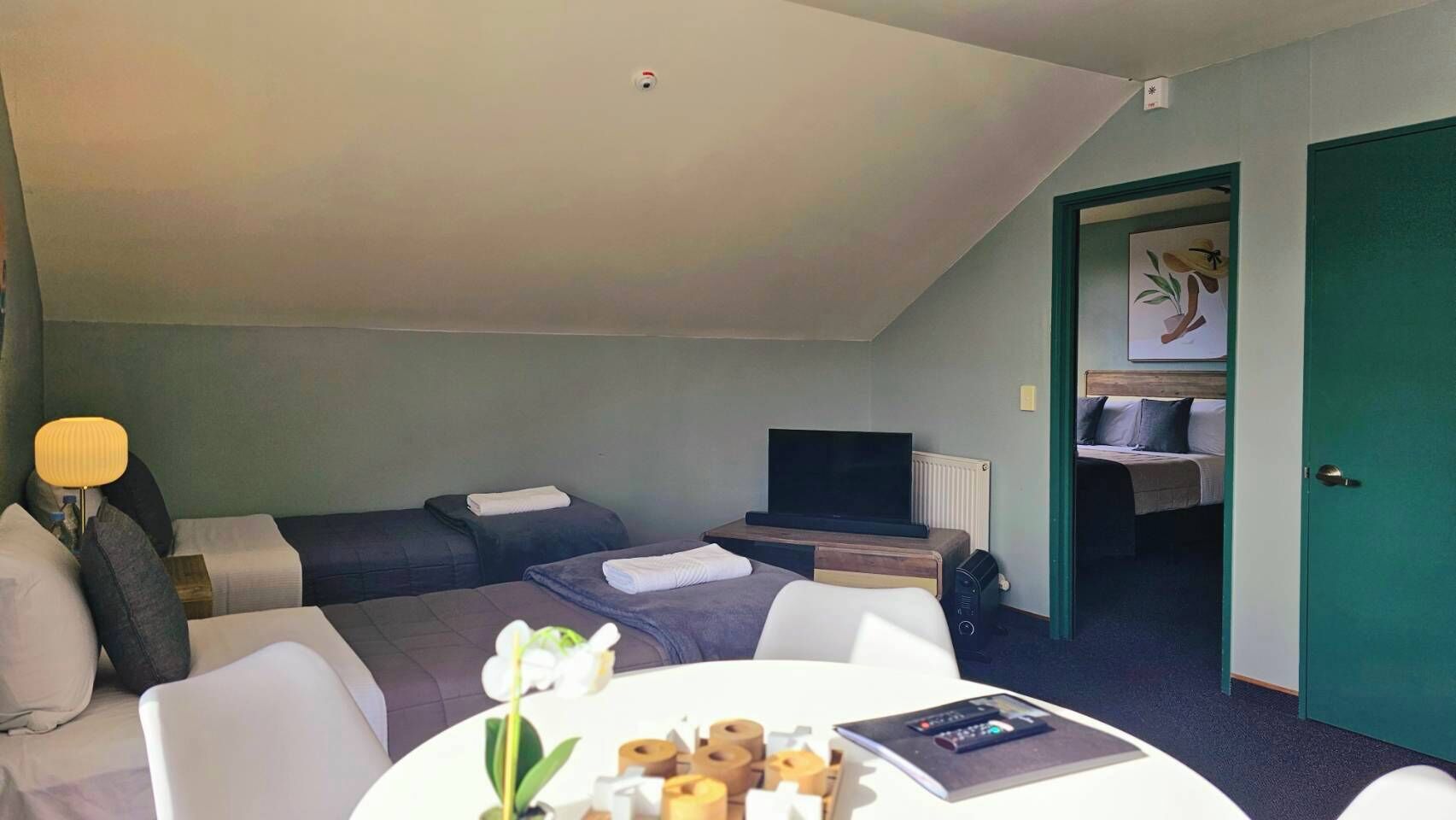 Une chambre d’hôtel avec deux lits, une télévision, un bureau avec une lampe et une table à manger agrémentée d’un arrangement floral.