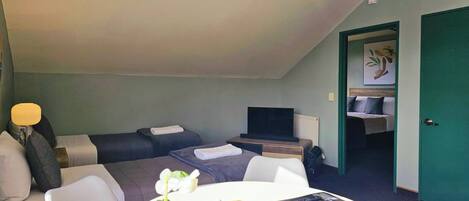 Une chambre d’hôtel avec deux lits, une télévision, un bureau avec une lampe et une table à manger agrémentée d’un arrangement floral.