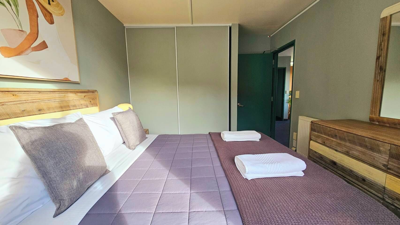 Una camera d'albergo con un letto, una testiera in legno, uno specchio e una porta che dà su un'altra stanza.