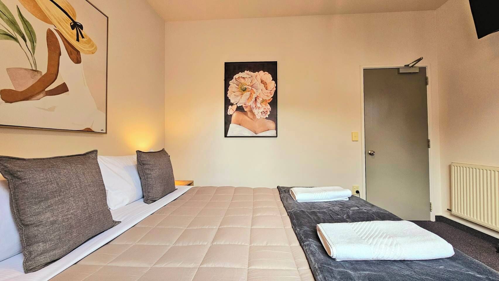 A hotel room with a large bed, two pillows, a painting on the wall, and a radiator.