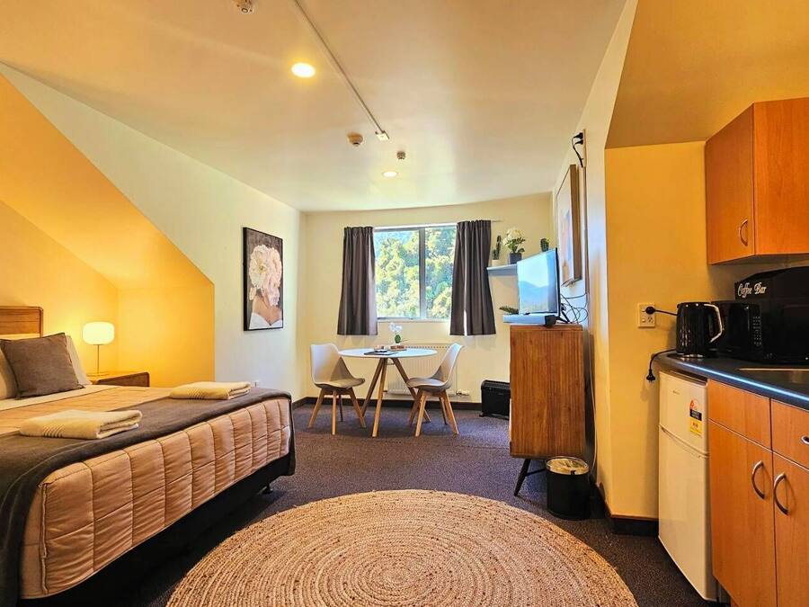 A compact hotel room with a bed, a small desk, a coffee machine, and a kitchenette.