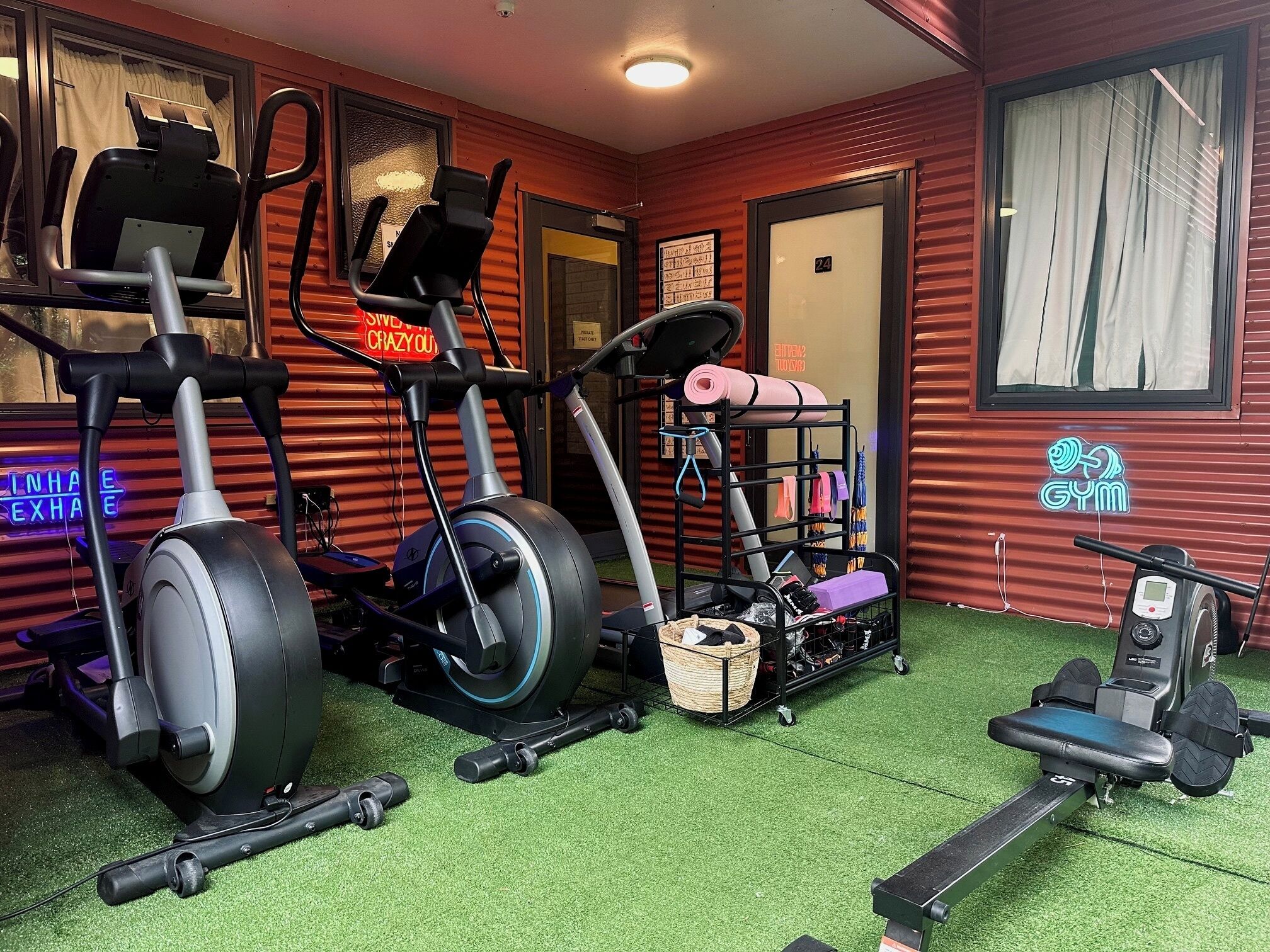 Ett gym med träningsutrustning, ett löpband och ett väggmonterat ställ med vikter.