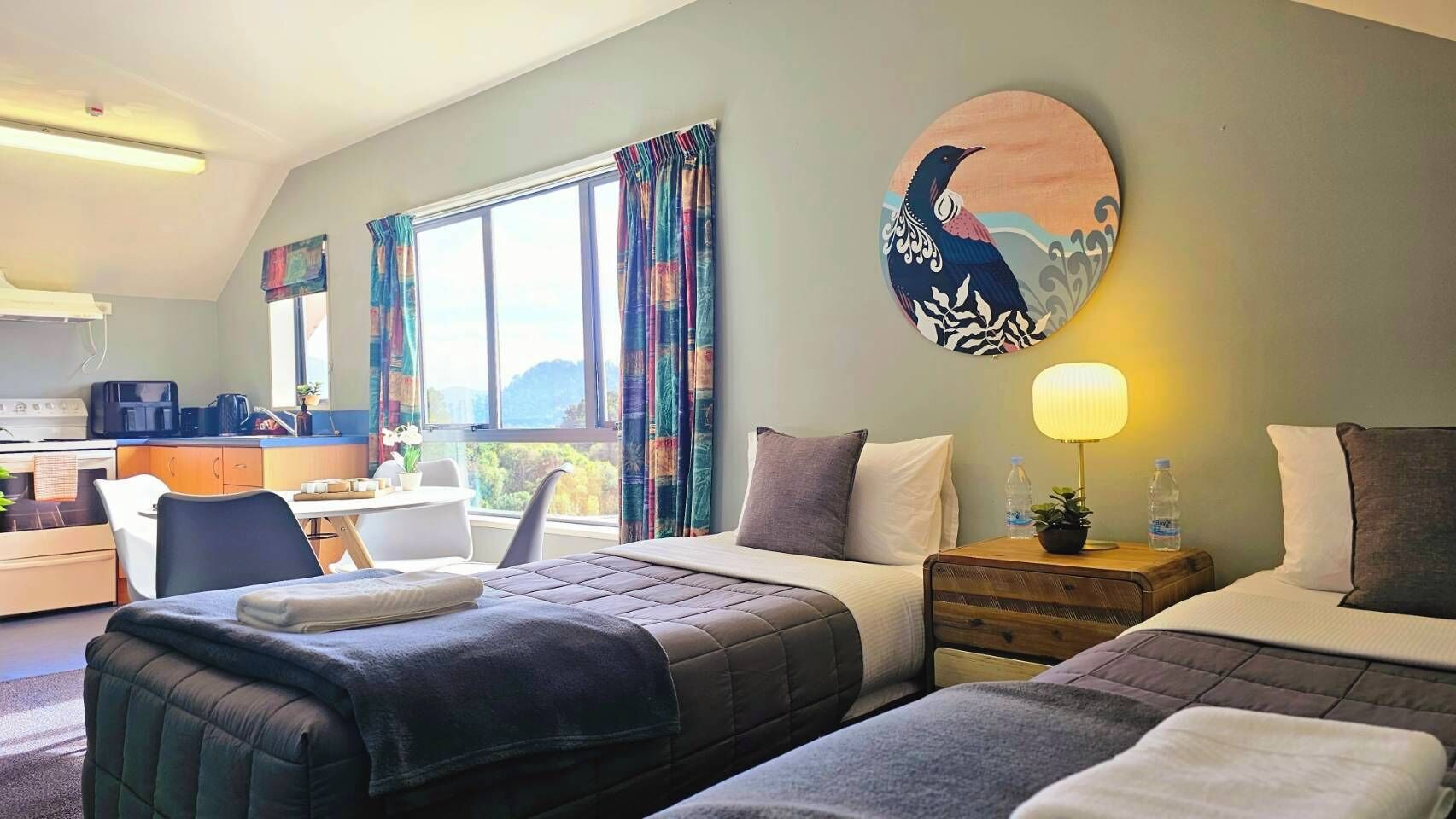 A hotel room with two beds, a dining area, and a view of the outdoors.