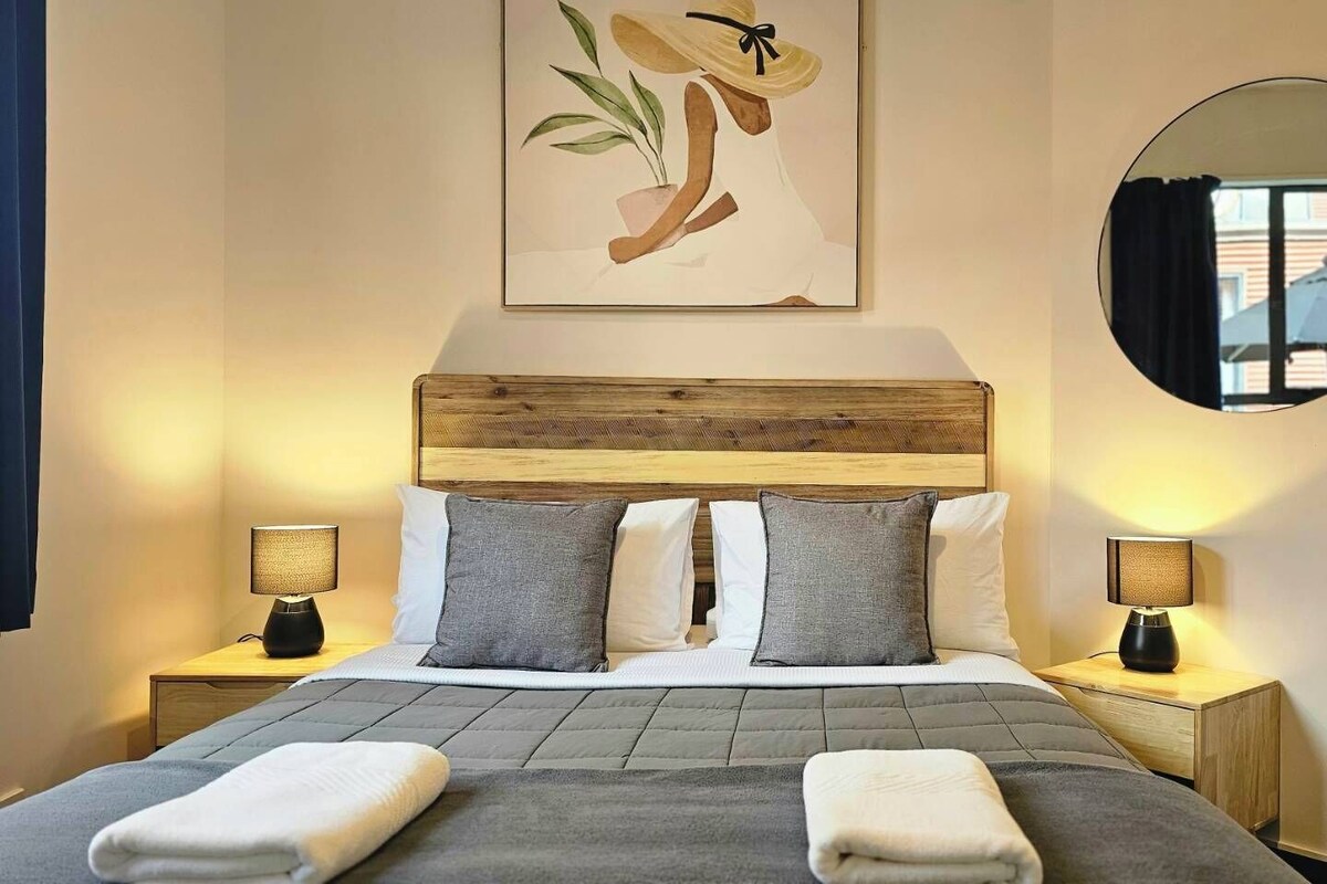 A hotel room with a bed, two bedside tables with lamps, a round mirror, and a wall-mounted artwork.