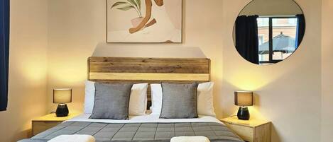 A hotel room with a bed, two bedside tables with lamps, a round mirror, and a wall-mounted artwork.