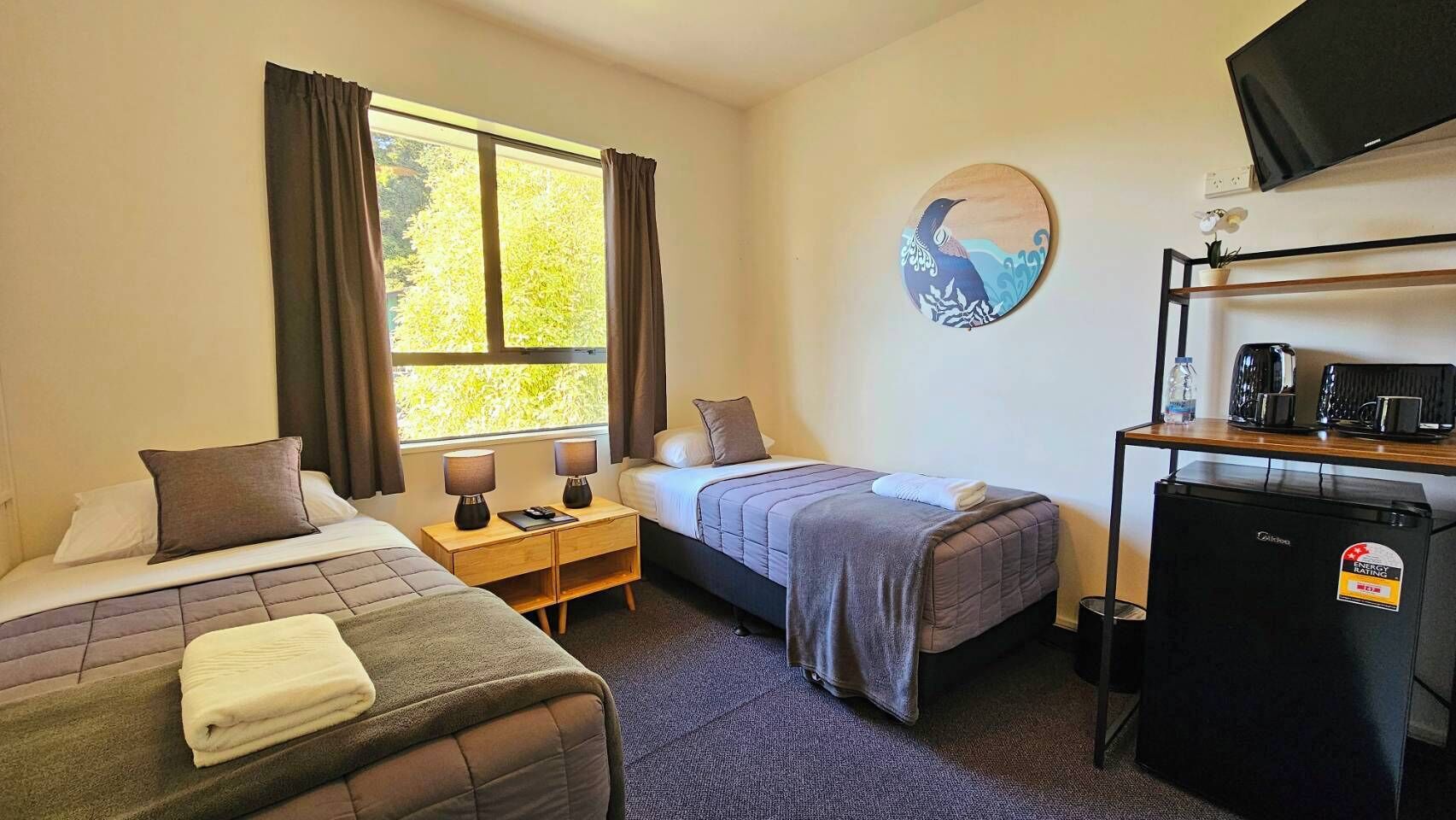 A hotel room with two beds, a desk, a refrigerator, and a window with curtains.