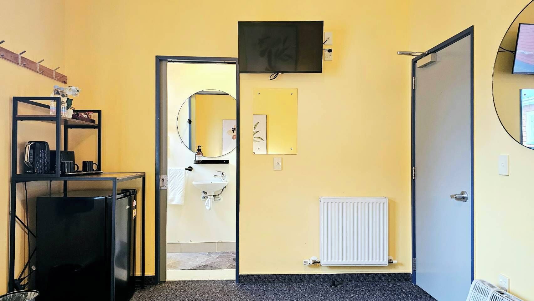 A room with a black desk, a white radiator, a door, and a mirror on the wall.