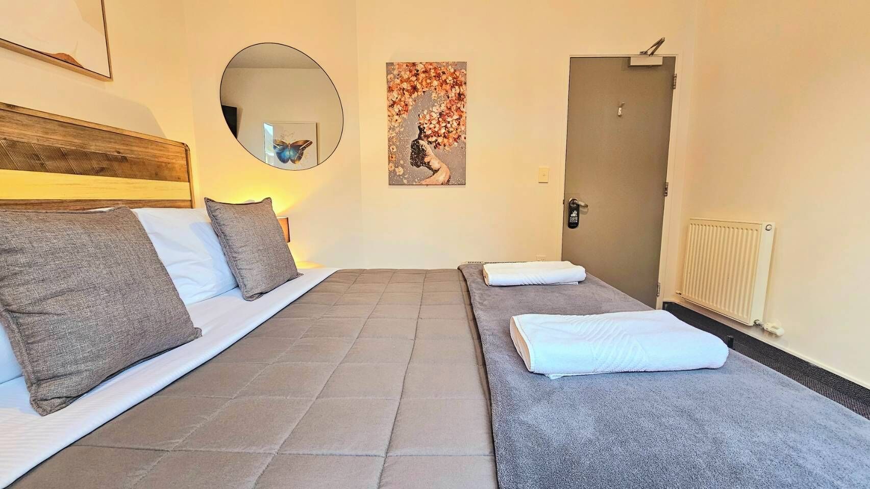 A hotel room with two beds, a mirror, a painting, and a door.