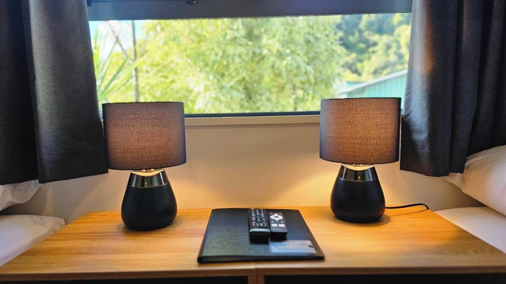 A wooden bedside table with two black lamps and a remote control.