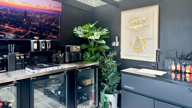 A modern kitchen with a large TV, a coffee machine, and a plant. - Wild Kea Lodge Franz Josef (Franz Josef Glacier)