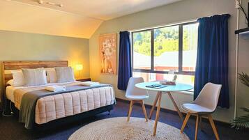 Une chambre d’hôtel avec un lit, une table ronde et deux chaises, une fenêtre avec des rideaux et un tableau au mur.