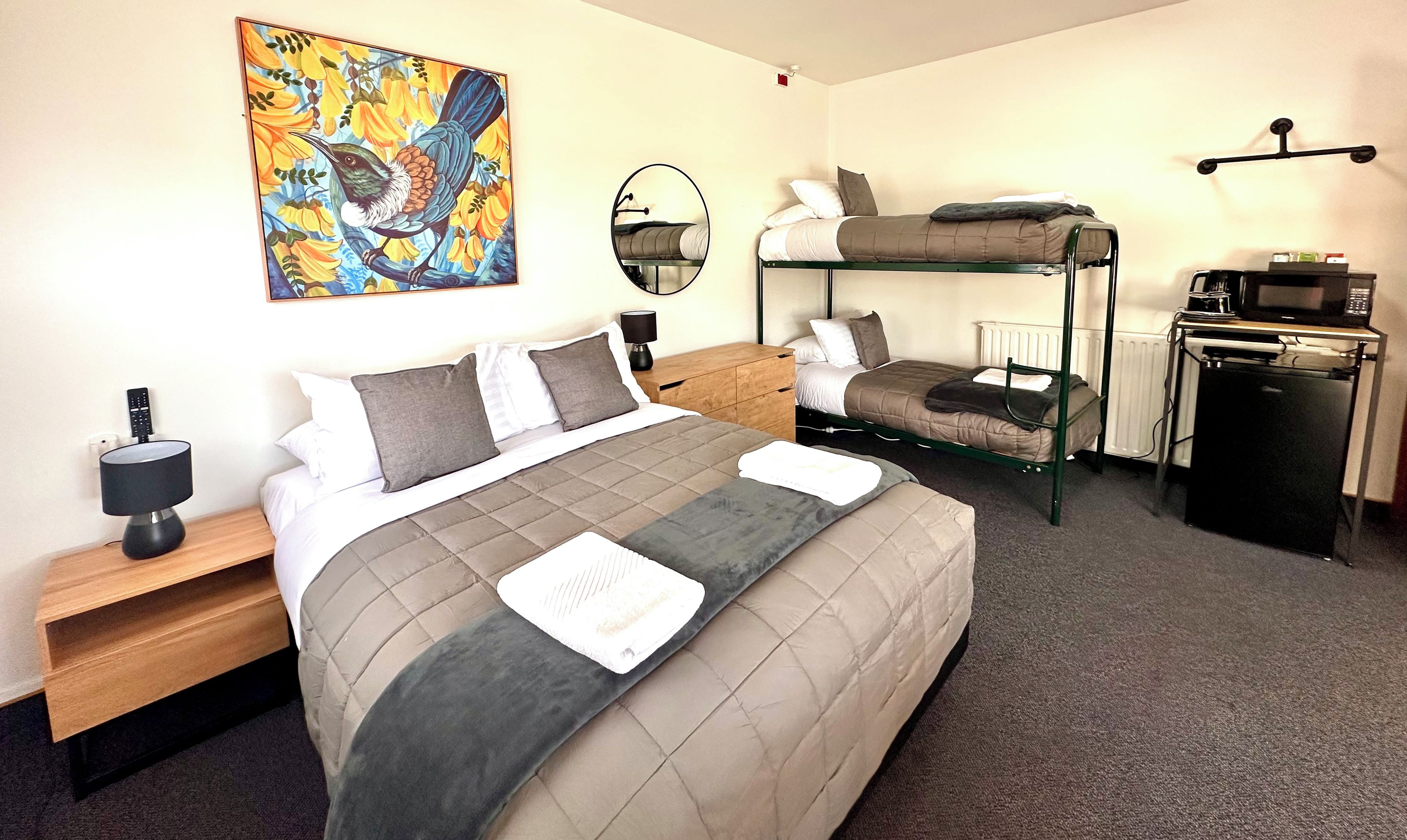 Una habitación de hotel con cama, literas, un escritorio con microondas y un cuadro en la pared.