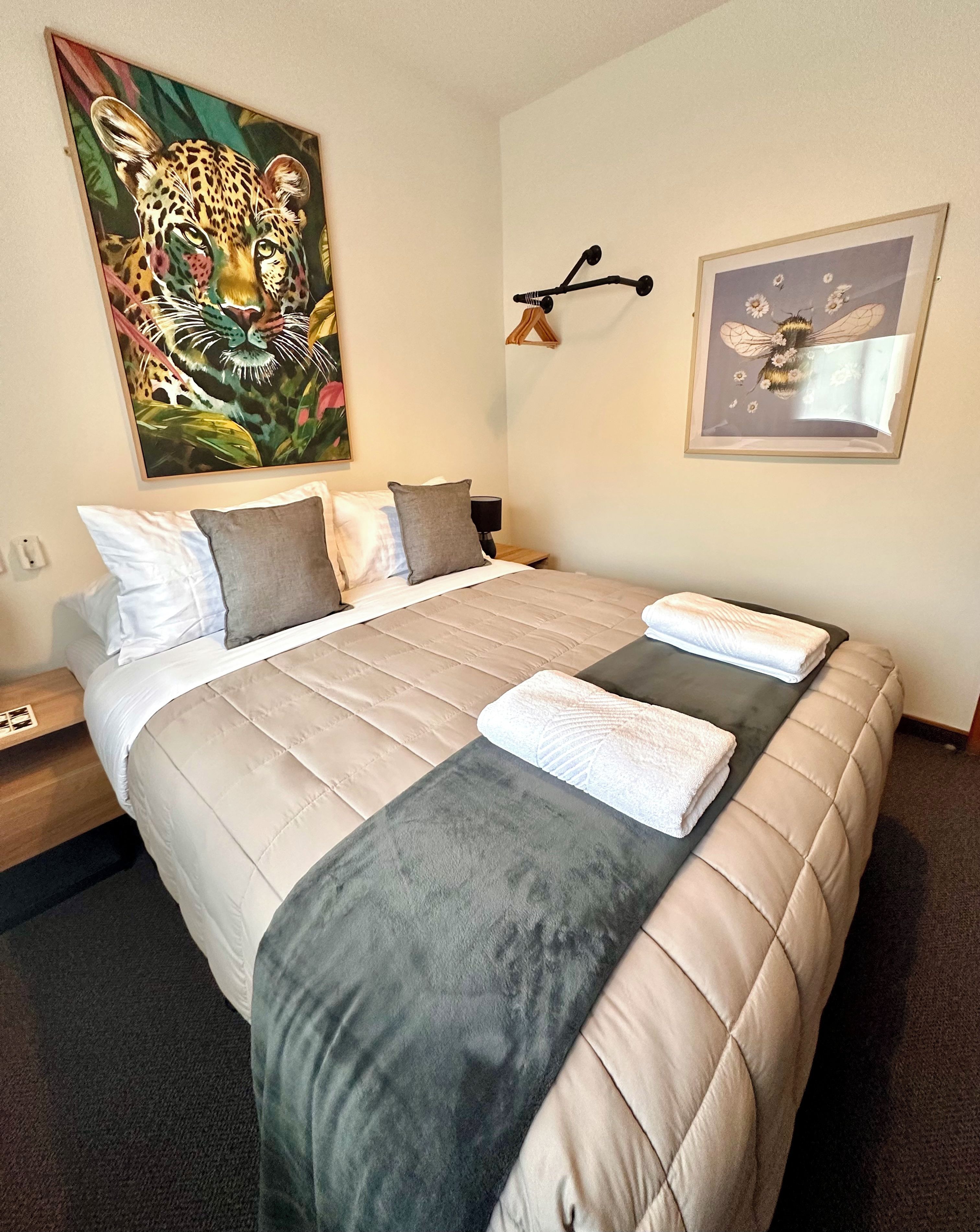 Une chambre d’hôtel avec un grand lit, un tableau représentant un léopard, une lampe fixée au mur et une œuvre d’art encadrée.