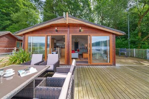 Een houten chalet met een glazen deur naar een woonruimte, een eettafel met stoelen, en een terras.