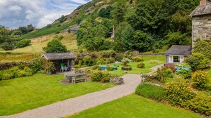 A rural house with a stone exterior, a gravel path, and a garden with various plants and flowers. - Broad How -  Large house ideal for families or walking groups. (Patterdale)