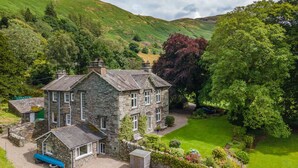 A stone house with a well-maintained garden, a bench, and a car parked outside. - Broad How -  Large house ideal for families or walking groups. (Patterdale)