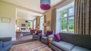 A living room with a grey sofa, two armchairs, a colorful rug, and a large window with curtains. - Broad How -  Large house ideal for families or walking groups. (Patterdale)
