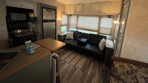 Une cuisine compacte intégrée dans le camping-car, équipée d’une cuisinière, d’un four à micro-ondes et d’un réfrigérateur. On y trouve également une petite table à manger et un canapé avec des coussins.