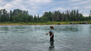 Une personne se tient dans une rivière, tenant une canne à pêche.